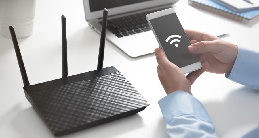 Man holding a smartphone at a desk next to a wireless router.